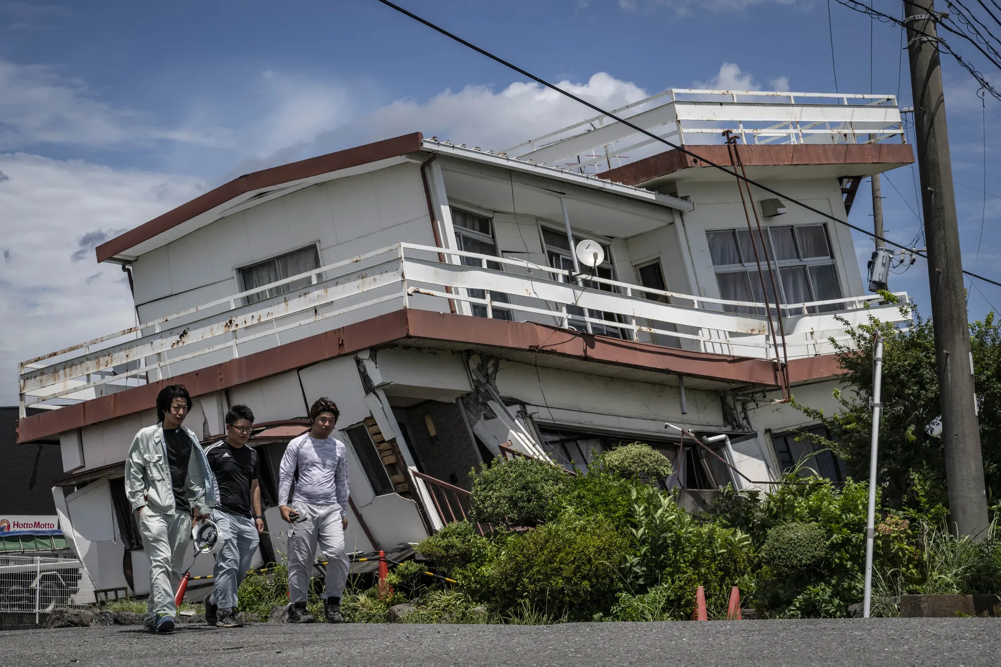 Para pekerja berjalan melewati sebuah rumah yang rusak dan sebagian runtuh di Yatsushiro, Prefektur Kumamoto pada Rabu (29/7/2026) setelah gempa bumi melanda Jepang barat daya pada hari sebelumnya.